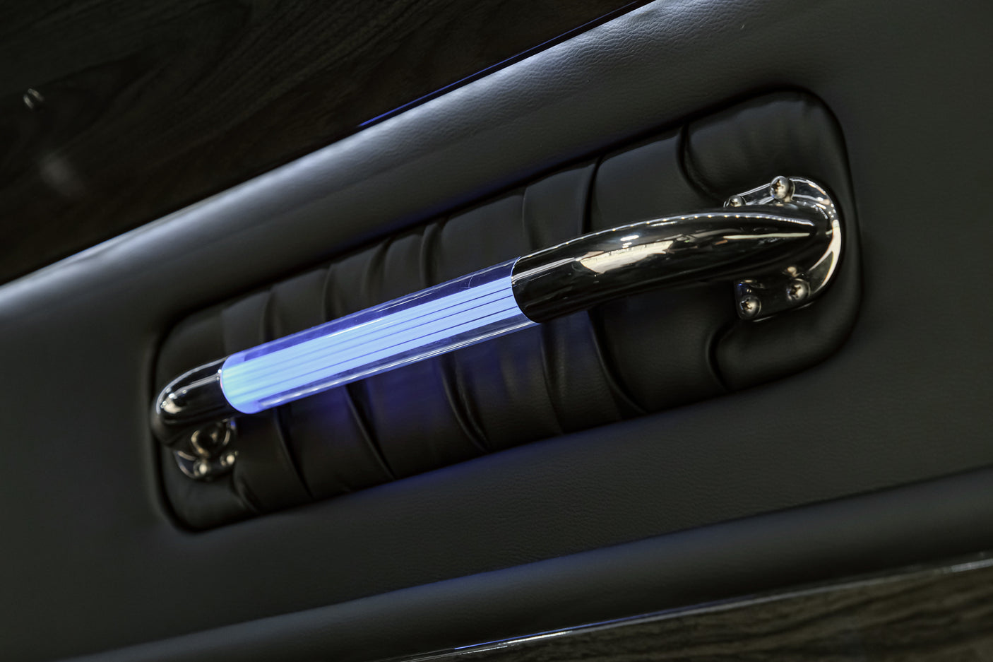 Luxury RV rental interior: black padded panel, with a chrome grab handle illuminated by a vibrant blue LED light.