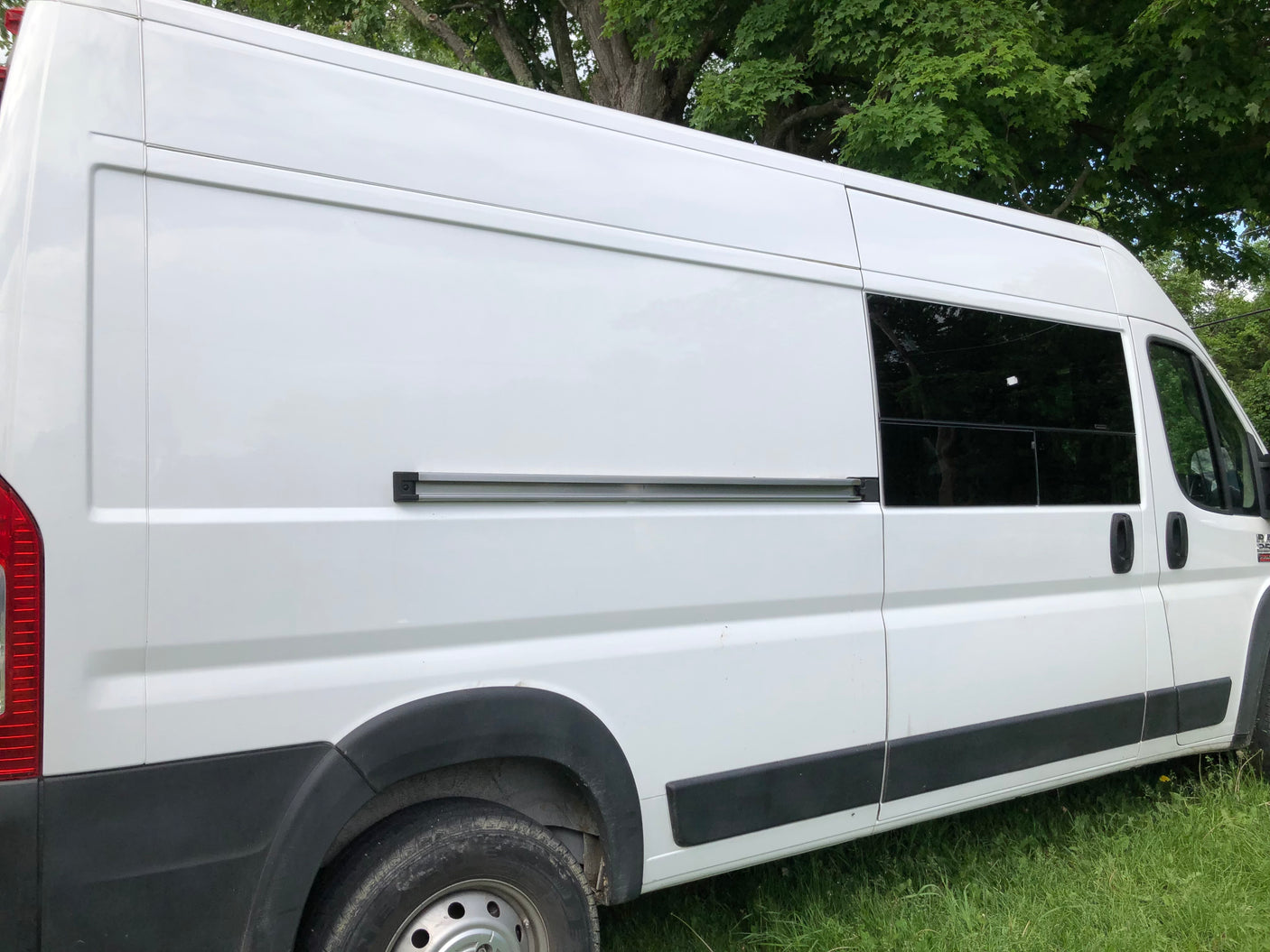 White camper van, perfect for an RV rental. Side view shows tinted windows and a side door track, parked on green grass.