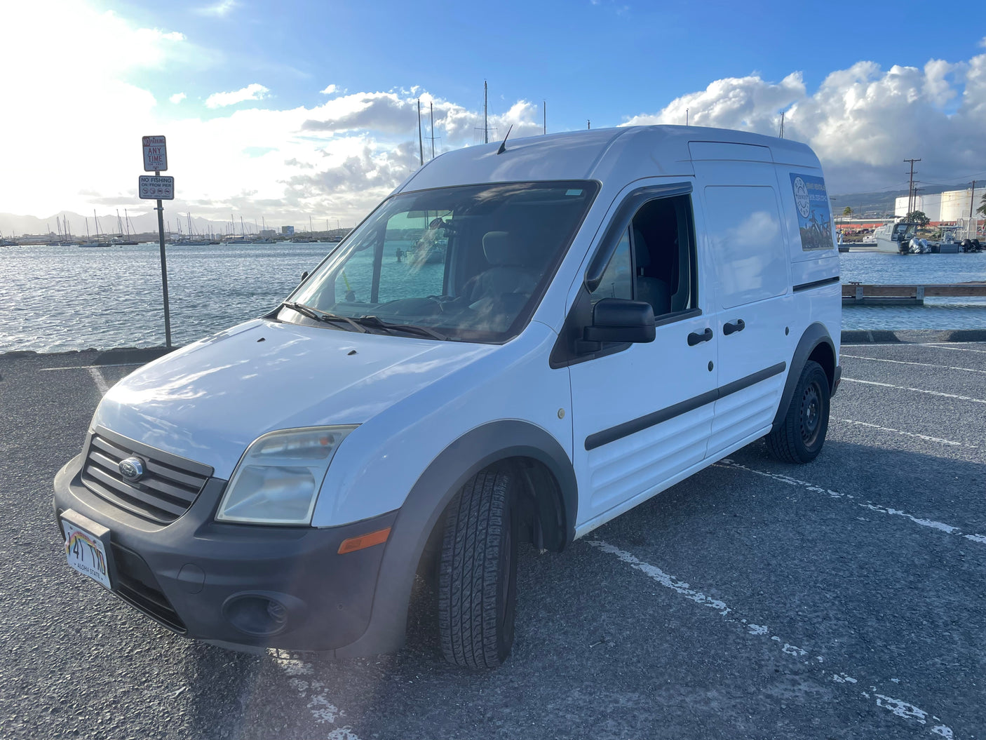 White Ford van for ebike rentals, similar to a small rv rental vehicle, parked by a sunny harbor.