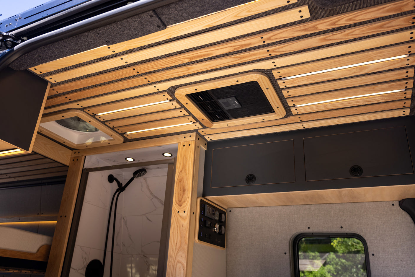 Inside a premium RV rental camper van: wood slatted ceiling, integrated lighting, AC, full shower, and control panel.