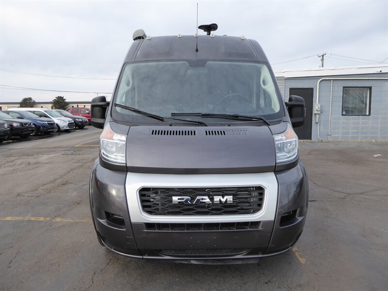 showing its exterior with an awning and running boards on asphalt.|Front view of a dark grey Ram ProMaster van