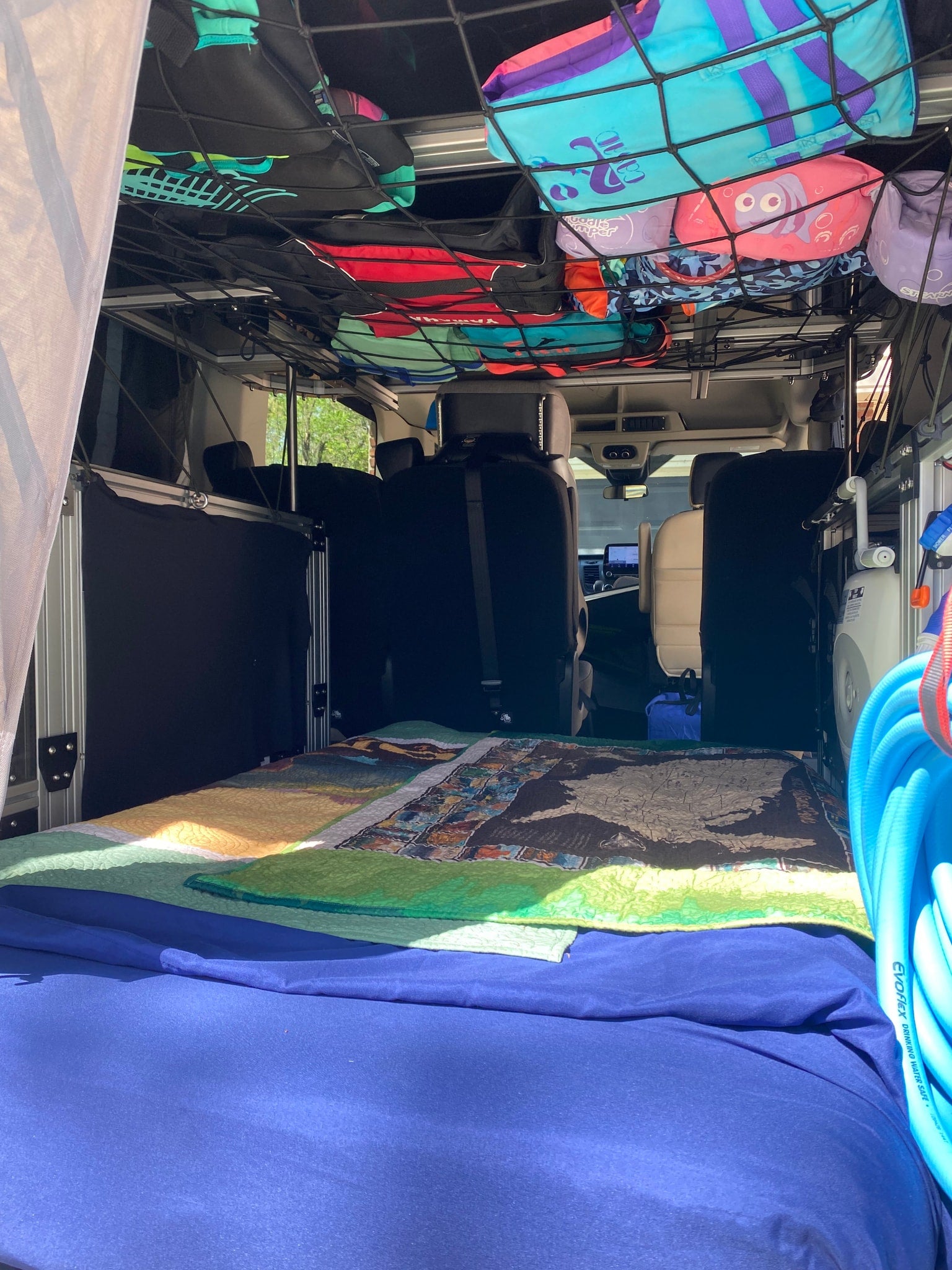 Inside an RV rental: a camper van interior with a bed, overhead net of life vests, and custom features.