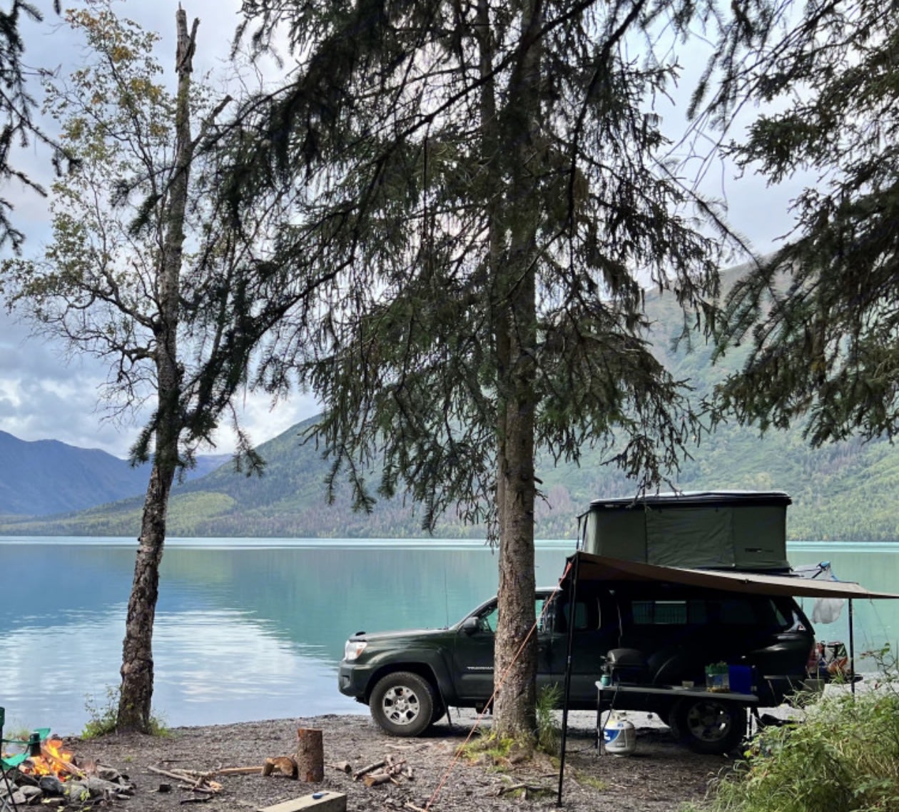 Scenic lakefront RV rental truck camping with a rooftop tent. Mountains and a campfire set the scene for wilderness adventure.