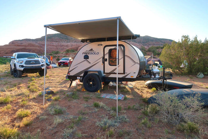 parked amidst a red rock desert landscape under a clear blue sky.|This FreeSolo teardrop RV rental is perfectly set up for desert camping