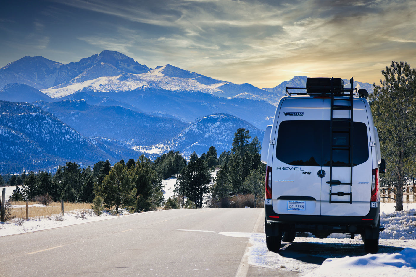 A Winnebago Revel rv rental is parked roadside with stunning snow-capped mountains. Ideal for a winter adventure!