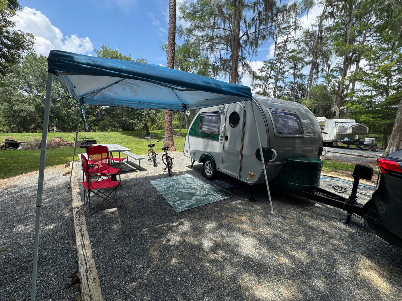 Perfect RV rental campsite setup! A sleek travel trailer, picnic table, and bikes under a canopy on a gravel spot. — photo 9