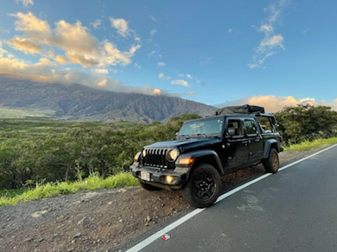 Black Jeep Gladiator w/ rooftop tent on a scenic mountain road. Ideal rv rental for your next outdoor adventure.