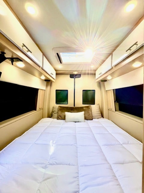 and overhead lighting for comfort and style.|Explore by RV rental! A blue camper van is parked lakeside under a cloudy sky