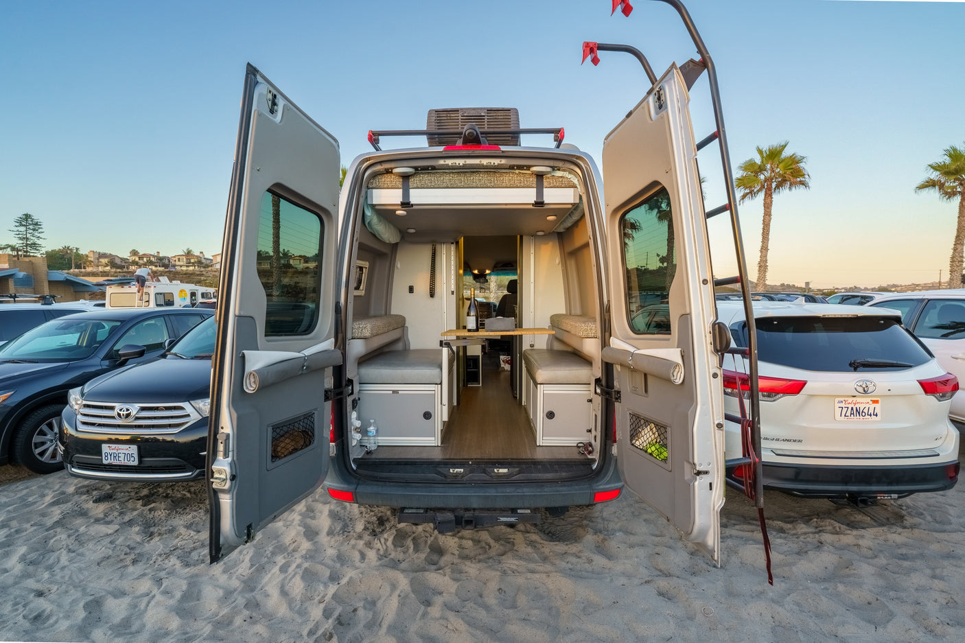 Open doors of an RV rental on a sandy beach, revealing a customized interior perfect for beach camping.