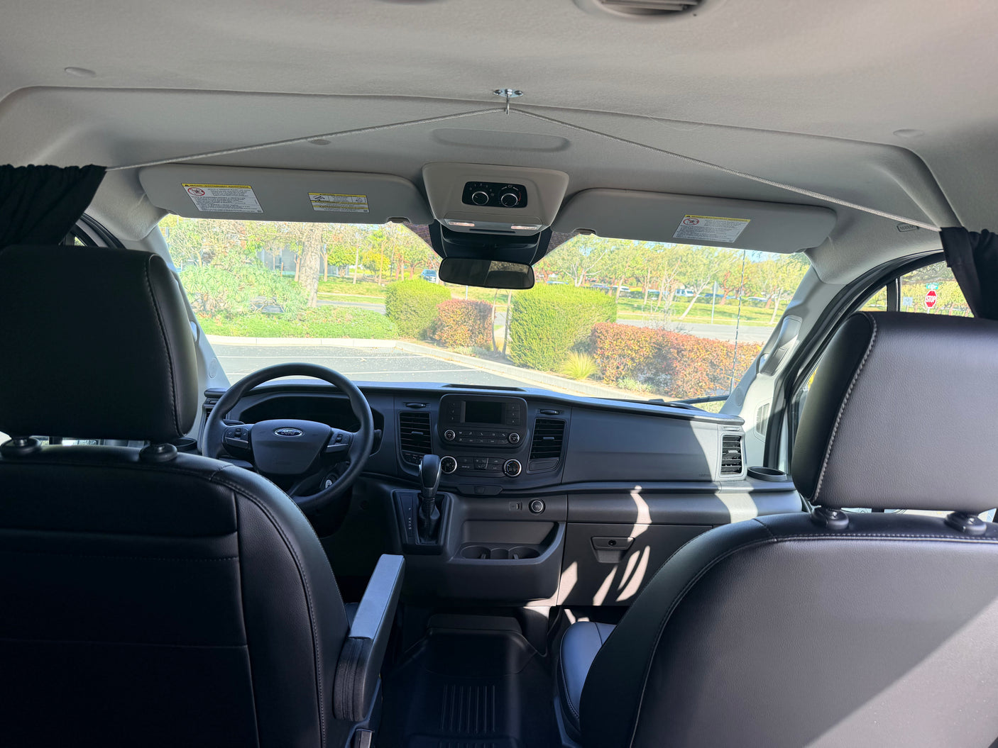 Modern rv rental van interior from the rear, showing the dashboard, steering wheel, front seats, and sunny road ahead.