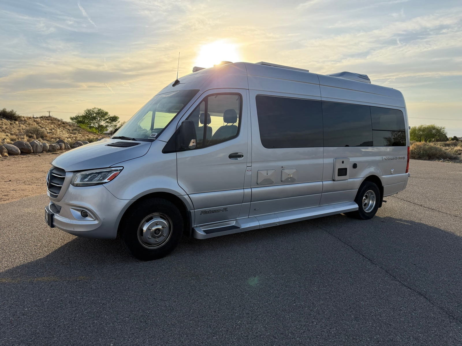 This sleek silver Mercedes Sprinter RV rental, a Pleasure-Way camper van, glows under a sunny sky, ideal for road trips.