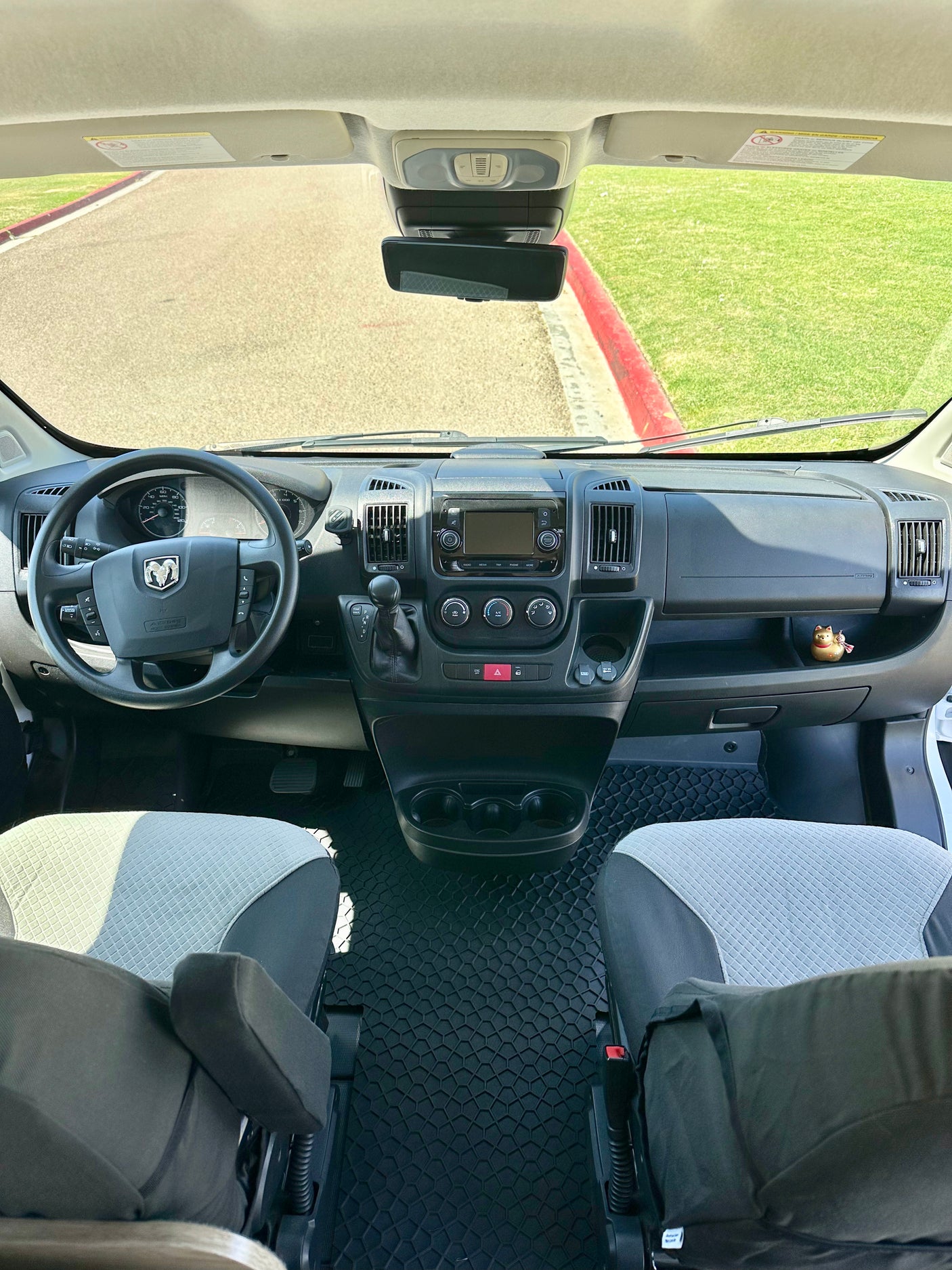 RV rental: Inside a modern camper van cockpit, showing the dashboard, steering wheel, and seats with hexagonal floor mats.