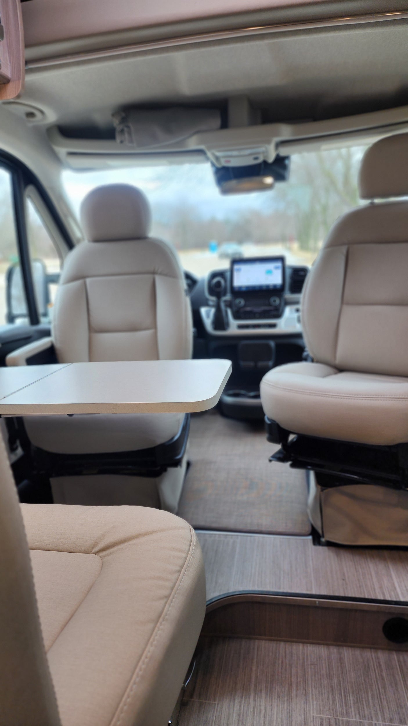 Interior of an RV rental showing comfortable beige seats, a table, and the driver's area with a screen.