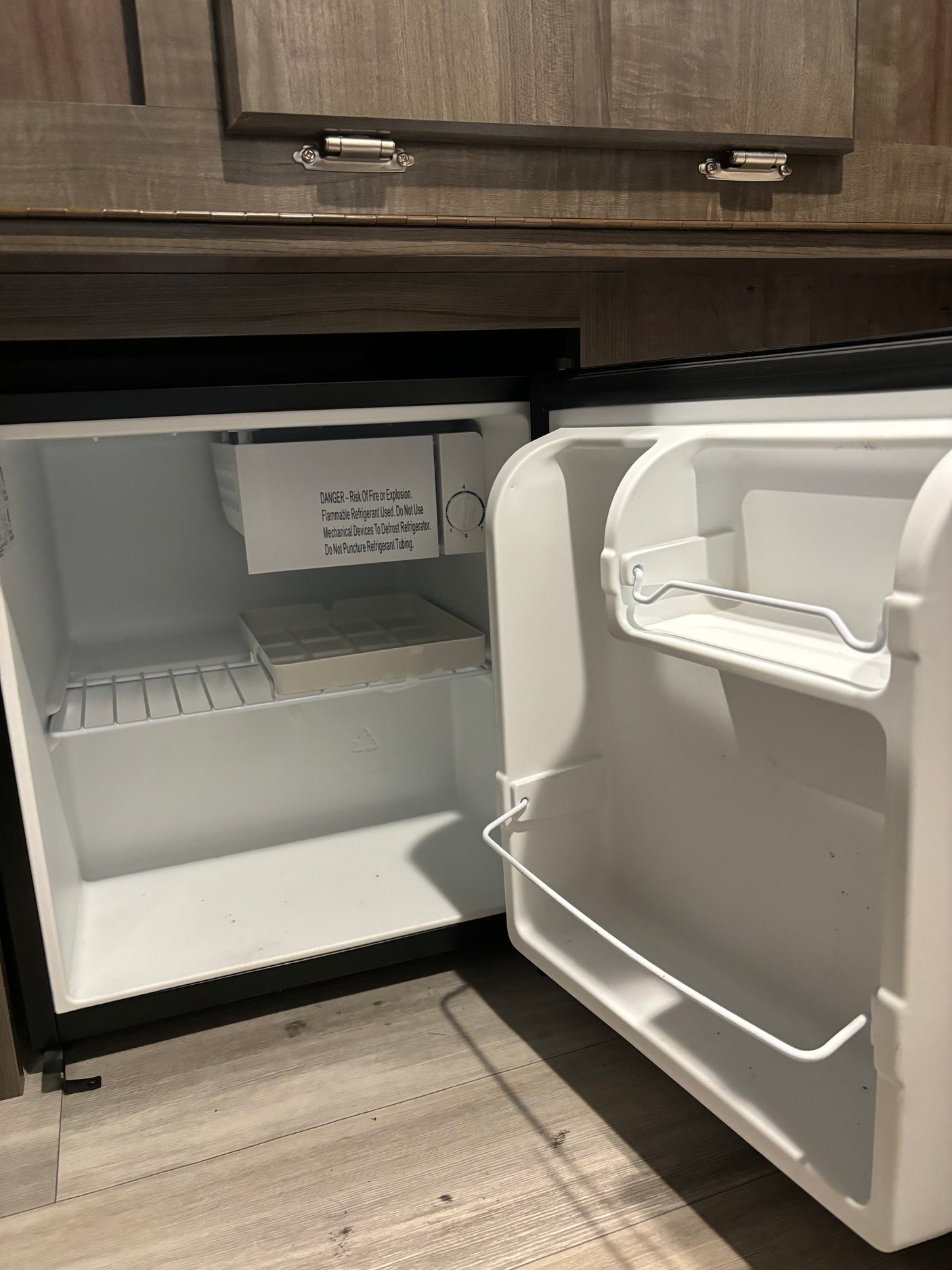 Inside an RV rental, a compact, open mini-fridge with white interior, wire shelf, and ice cube tray. Safety warning visible.
