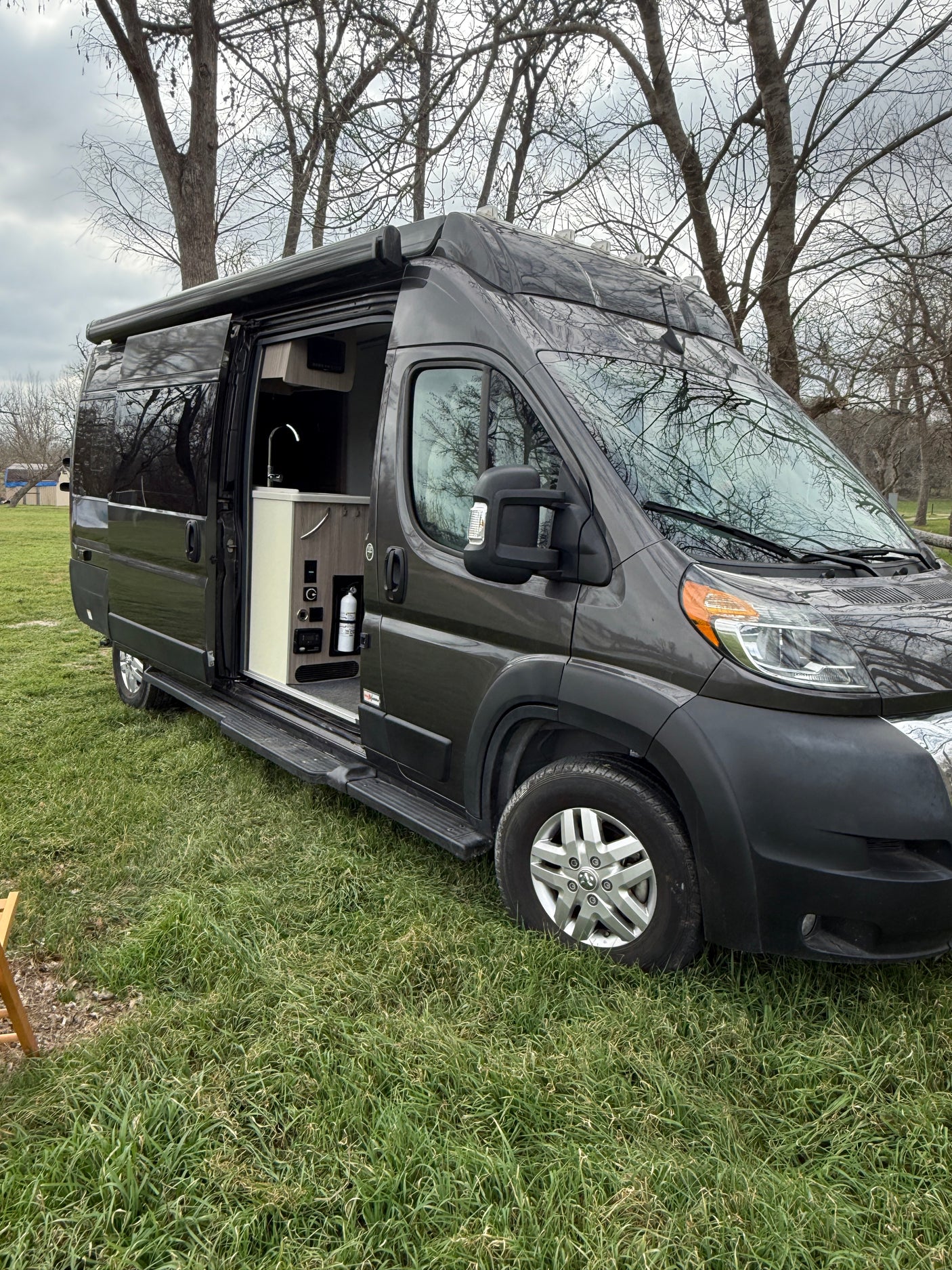 A sleek gray rv rental camper van, door open to a compact kitchen, parked on green grass, ready for your outdoor adventure.