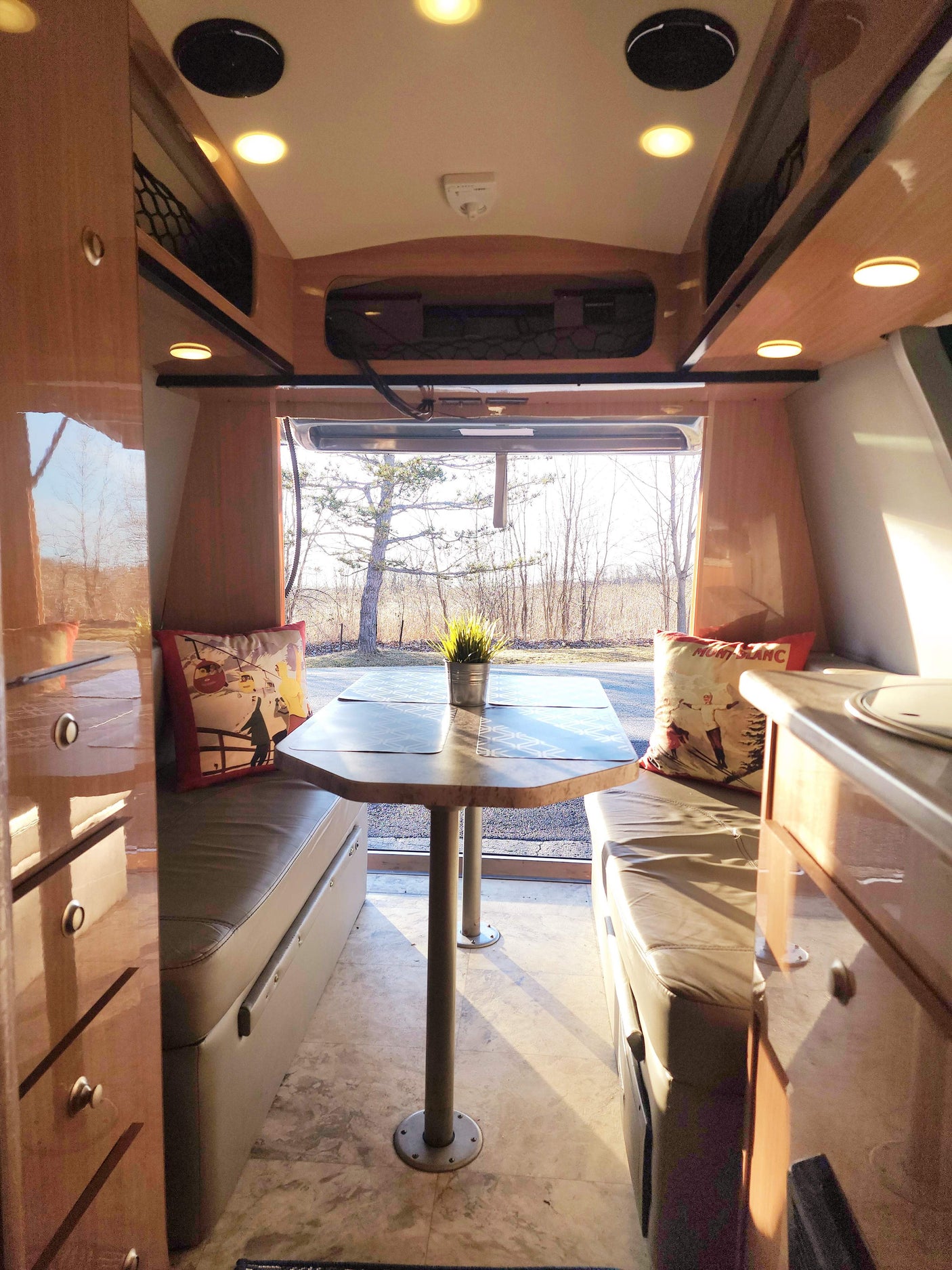 Cozy RV rental interior: A bright dinette with light wood cabinetry, comfortable benches, and a large window view for travel.