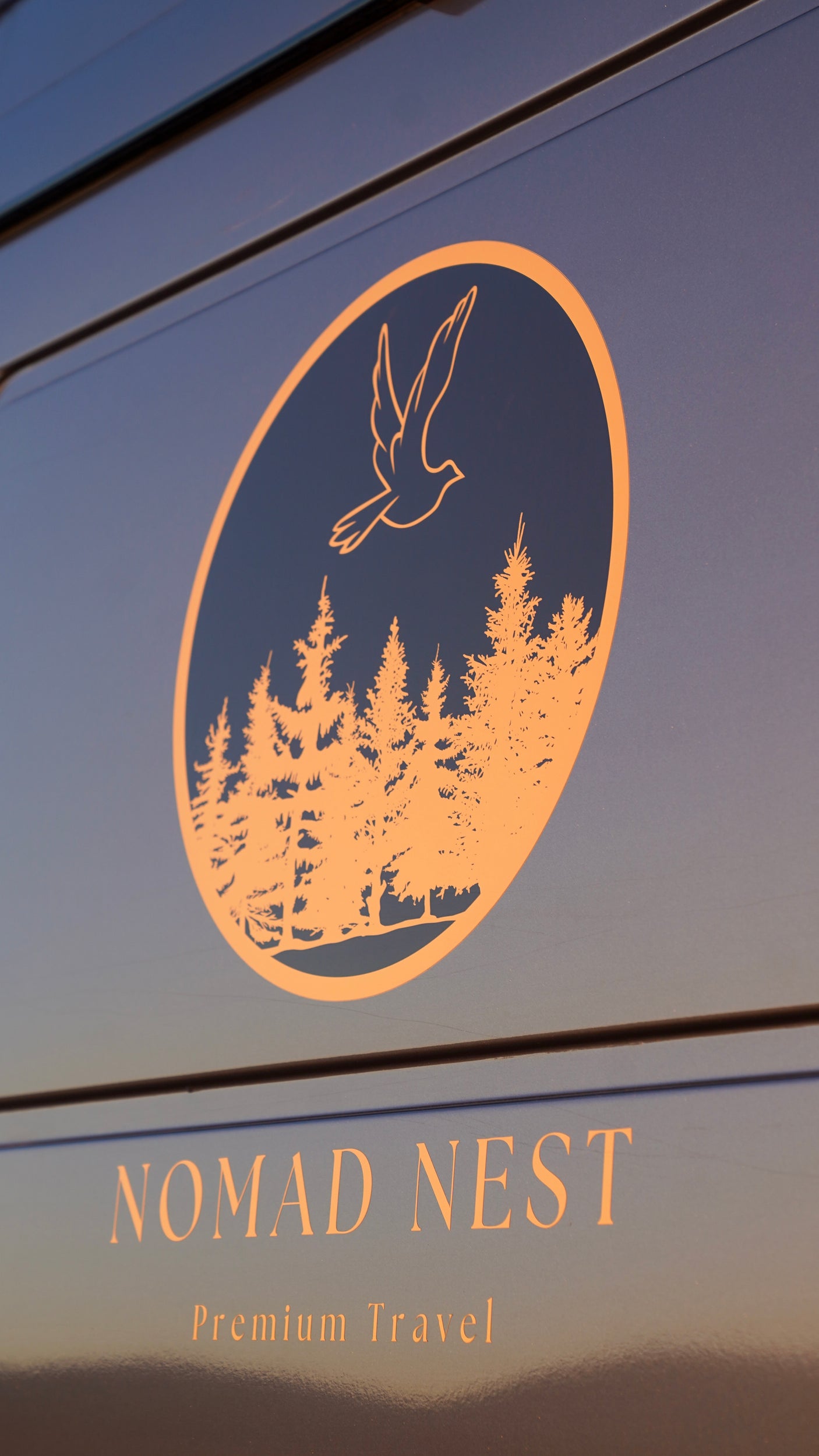 Close-up of a 'Nomad Nest Premium Travel' logo, golden bird and trees, on an RV rental vehicle side.
