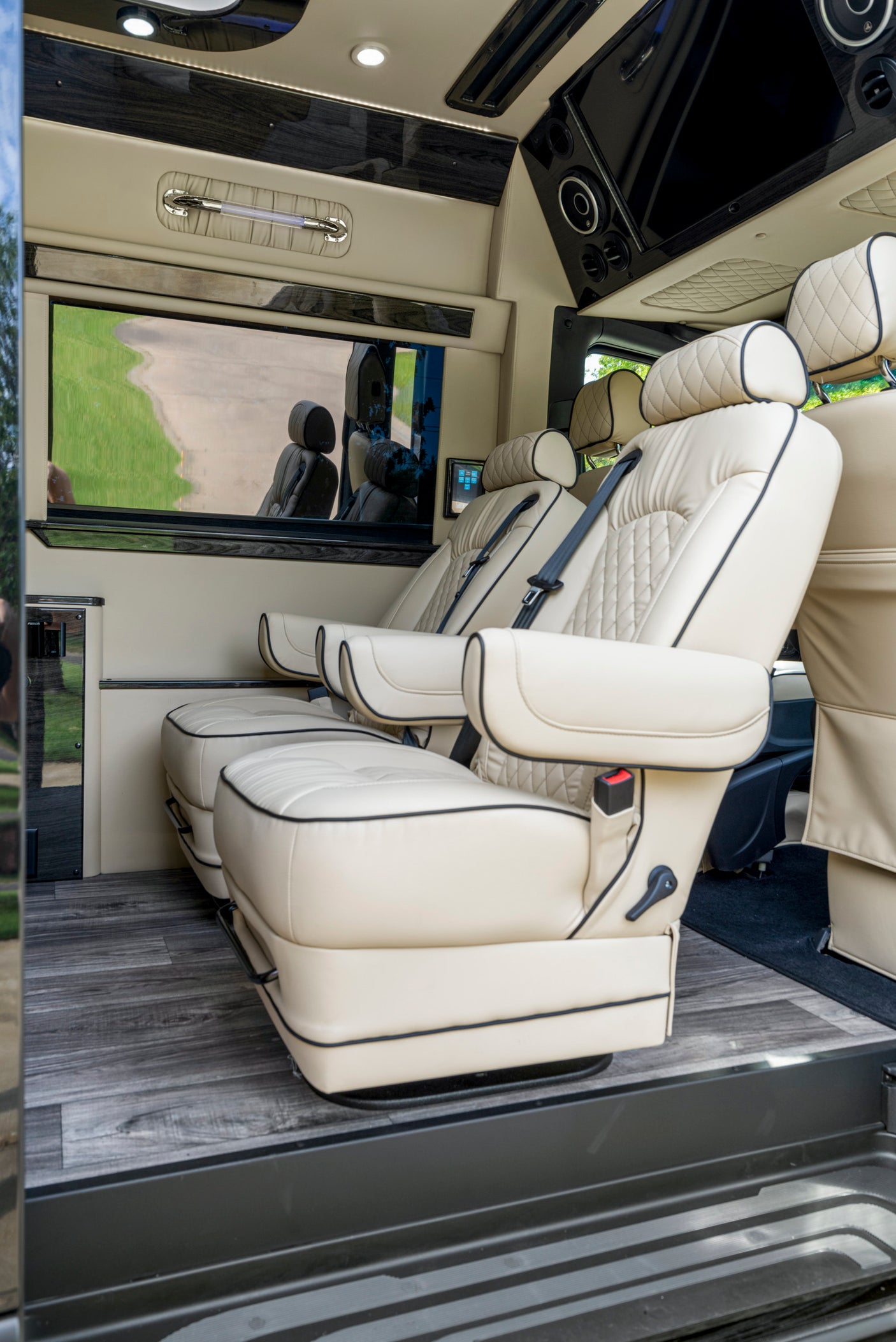 Plush interior of a custom RV rental, showing cream leather captain's chairs, wood floors, and entertainment system.