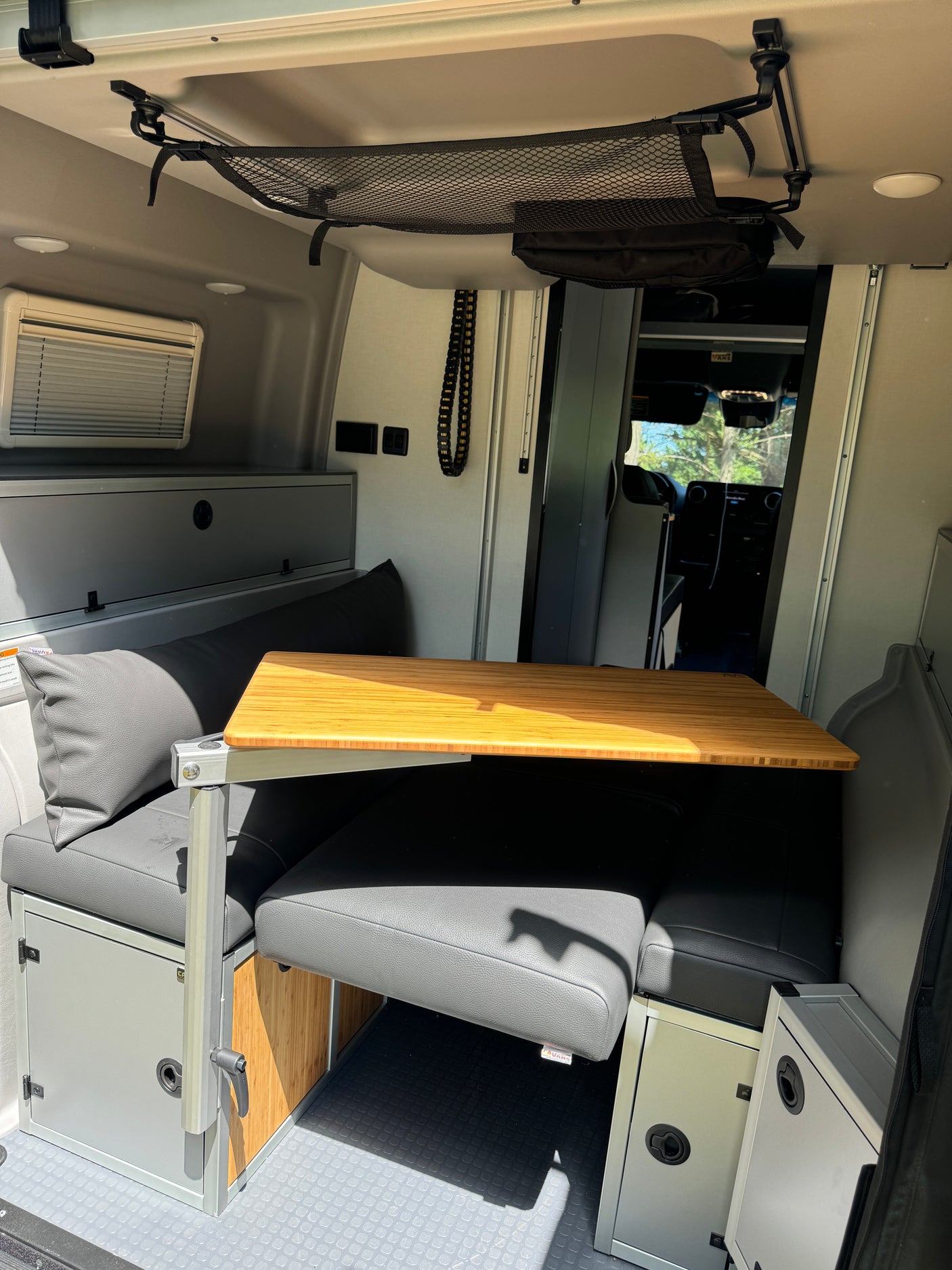 This RV rental features a compact interior dining area with a bamboo table, gray cushioned benches, and overhead storage net.