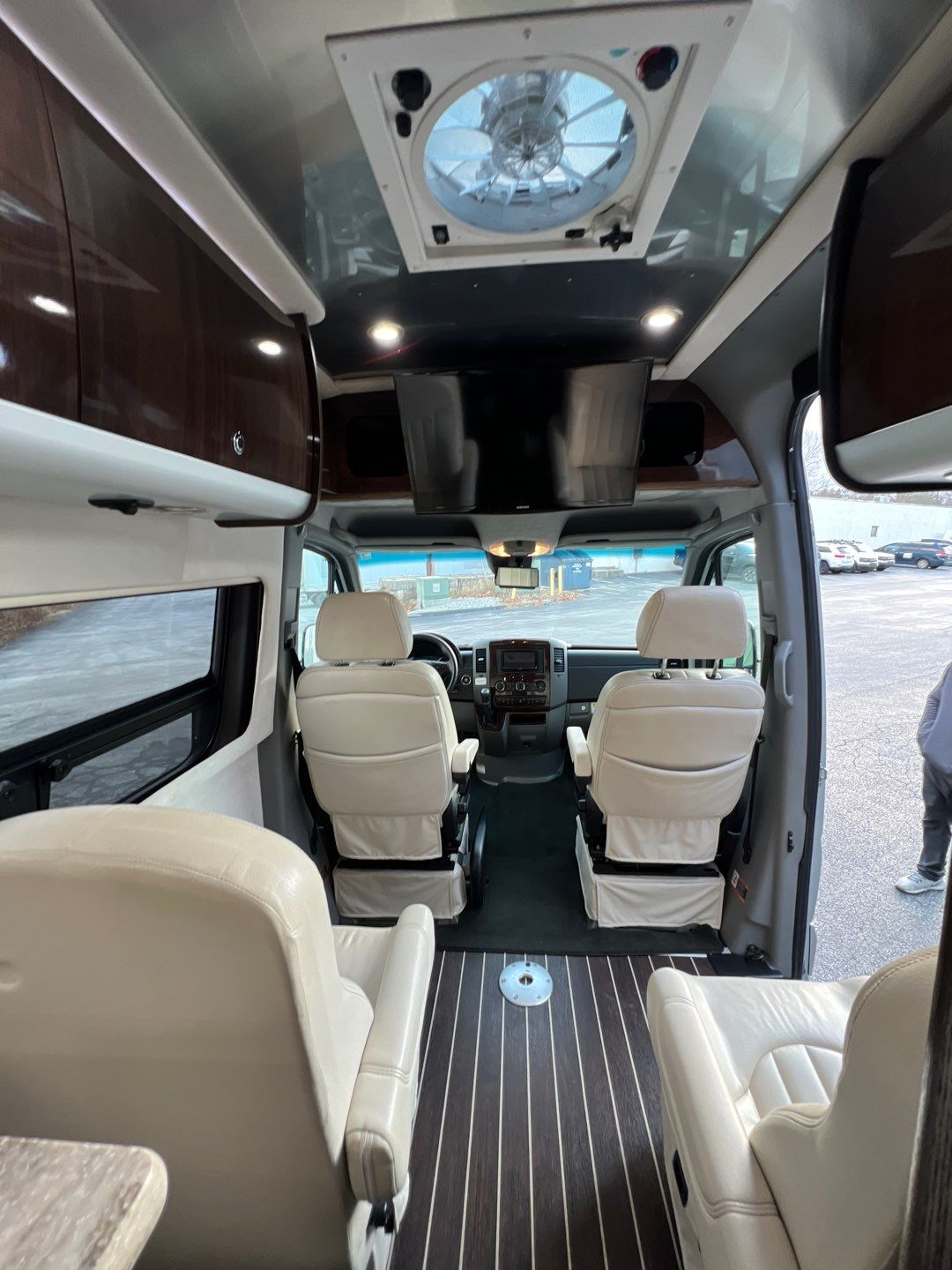 Luxurious RV rental interior: cream captain's chairs, wood floor, overhead storage & dual TVs. Ready for road trips.