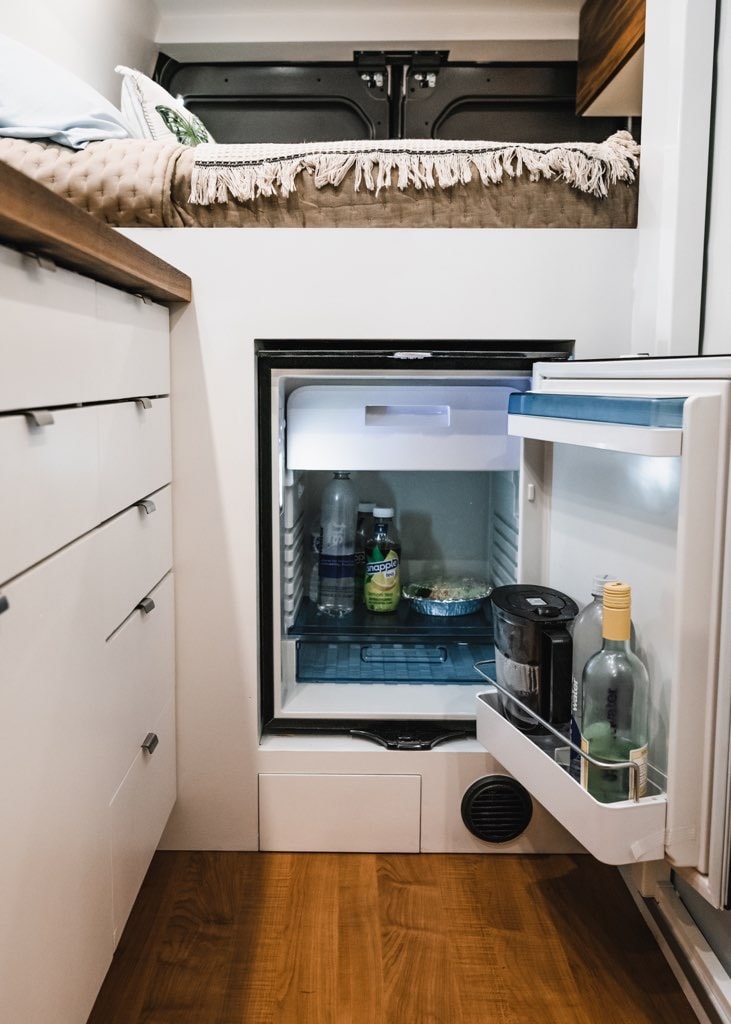 showing the cozy bed and kitchen. Thumbs up for van life!|Modern RV rental kitchen featuring a stylish sink with running water on a wood countertop