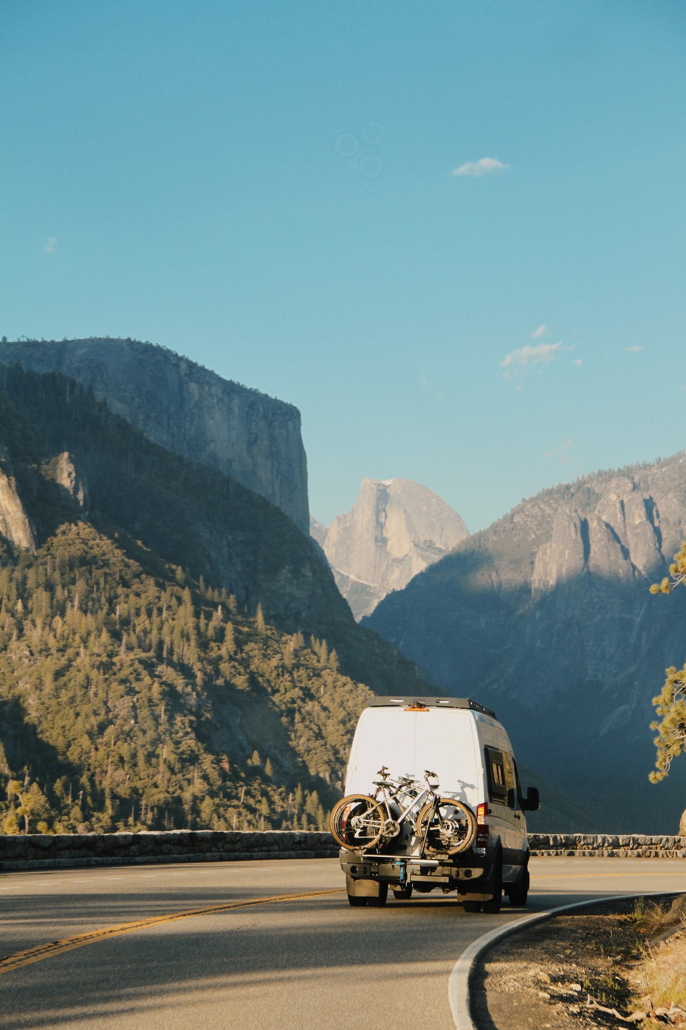 White RV rental with bikes on scenic road, passing iconic Half Dome in Yosemite.