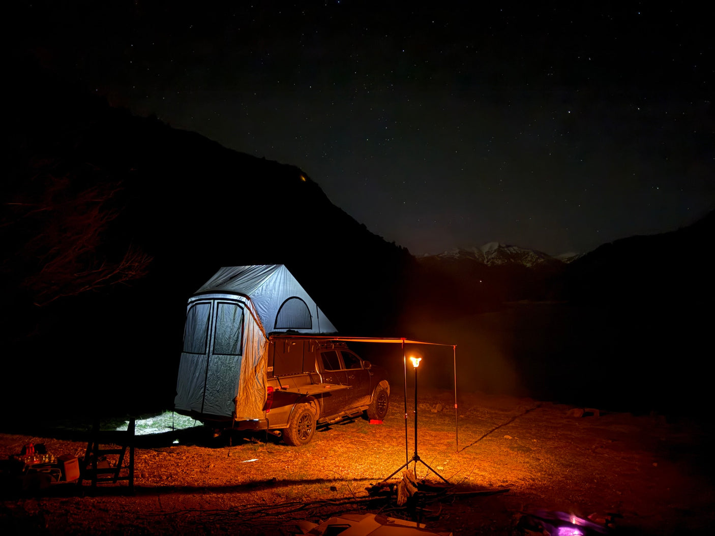 Starry night camping with a truck & rooftop tent, illuminated by warm light, mountains in view. Perfect rv rental for adventure!