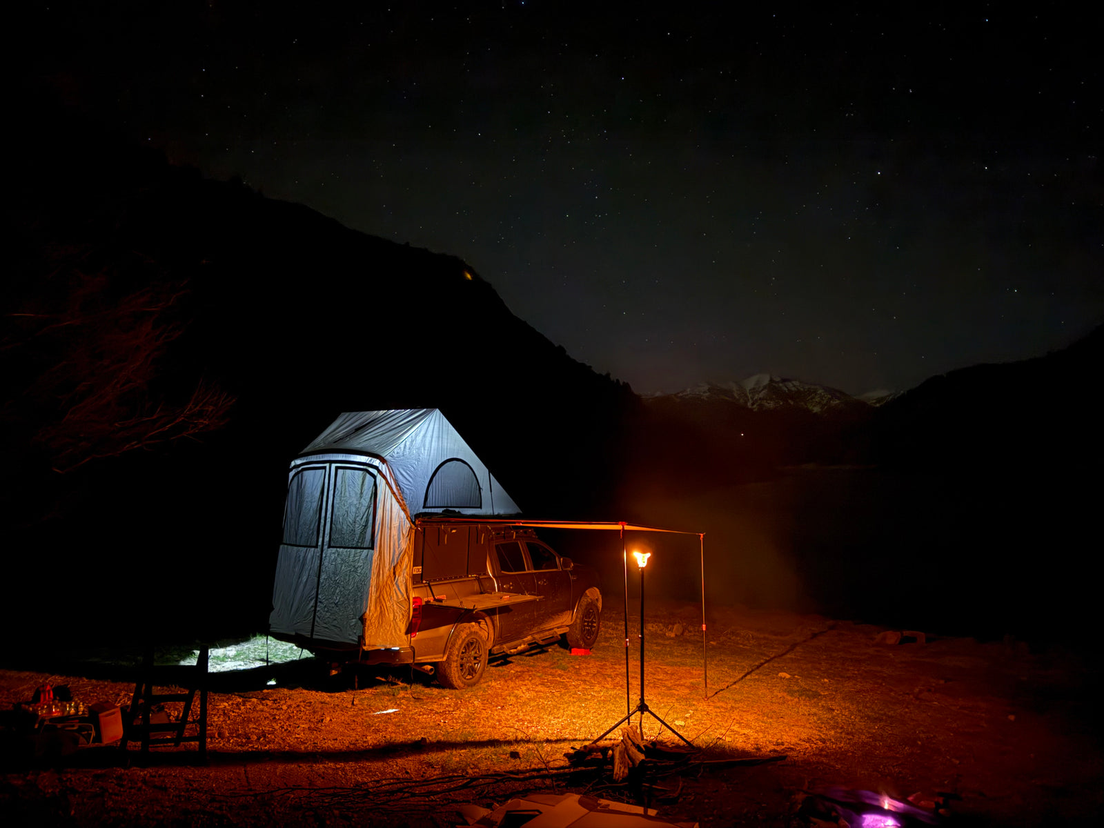 Starry night camping with a truck & rooftop tent, illuminated by warm light, mountains in view. Perfect rv rental for adventure!