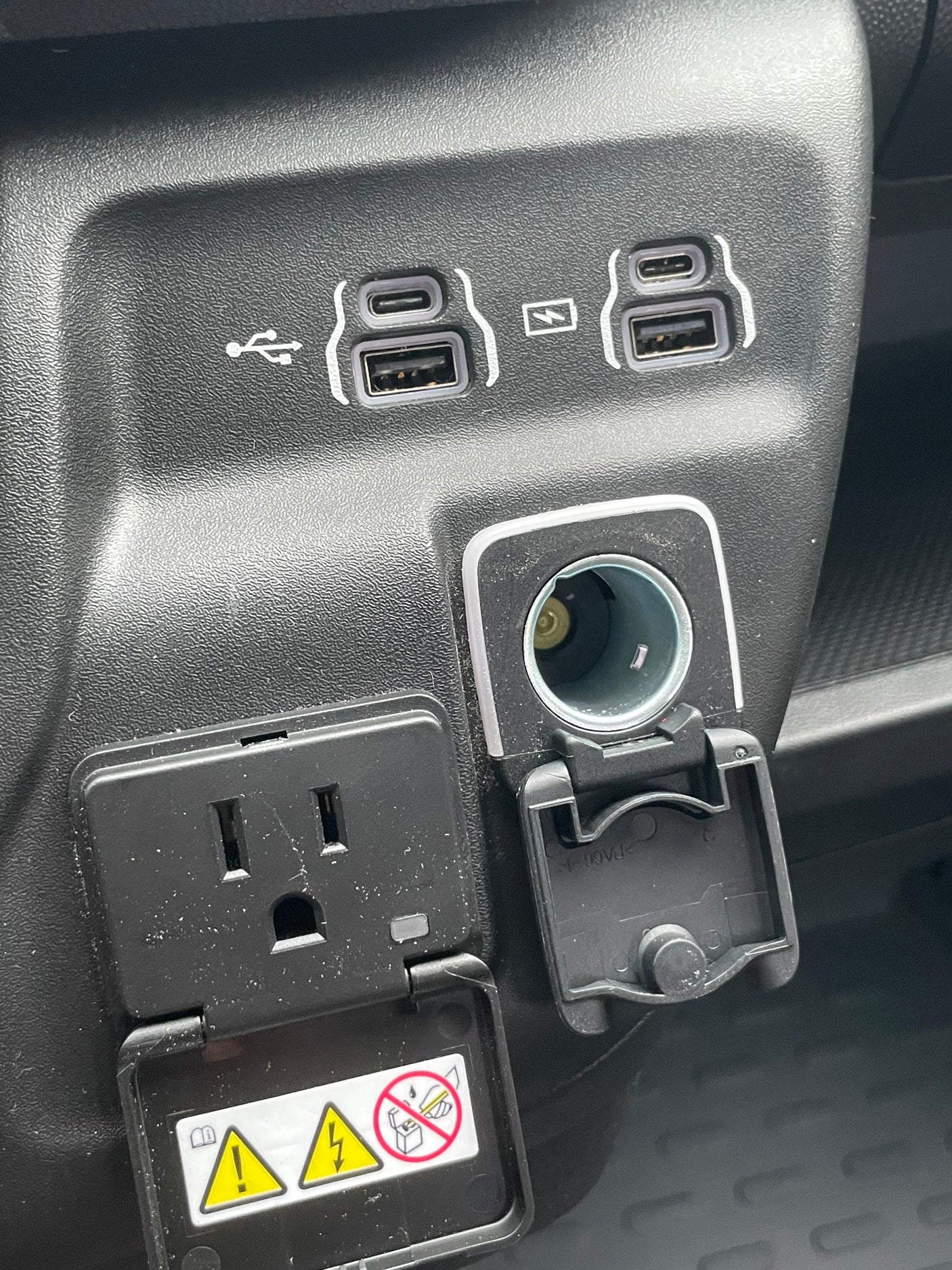 RV rental: Vehicle charging station with USB-A, USB-C, 12V, and a covered 110V AC outlet for electronic devices.