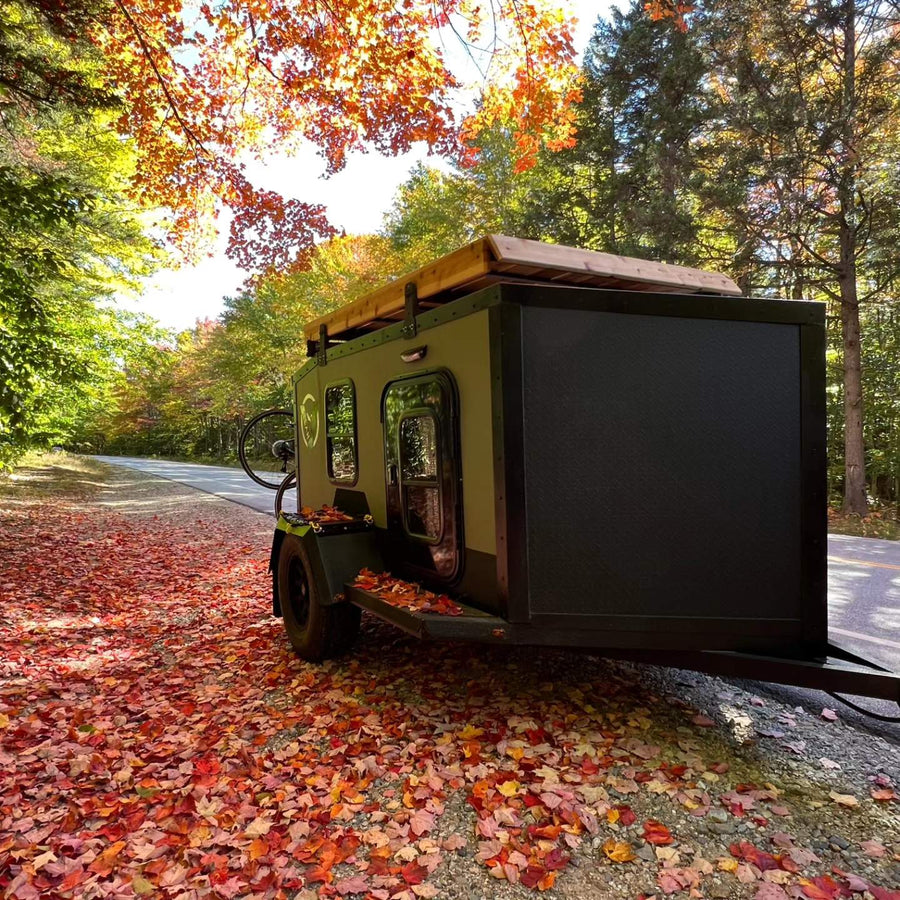 Autumn RV rental adventure! This compact trailer is parked amidst vibrant fall foliage & fallen leaves