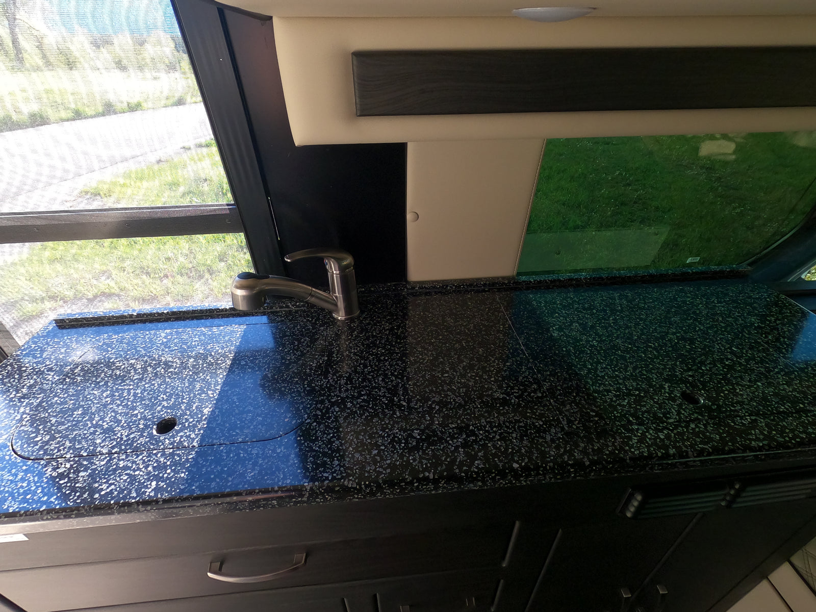RV rental kitchen with a black speckled counter, stainless steel faucet, and a window overlooking green scenery.