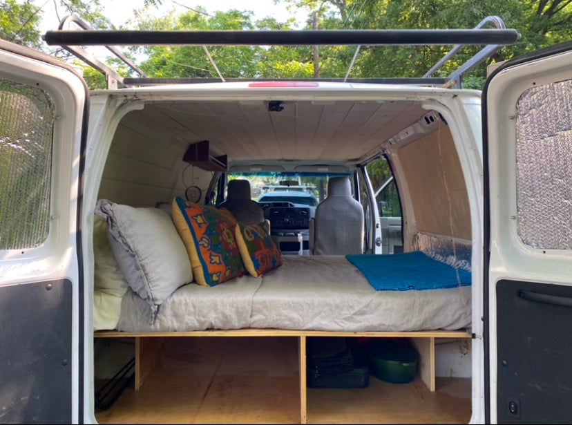 Inside this RV rental, a cozy van conversion features a bed over storage, facing the front seats. Ready for your road trip!