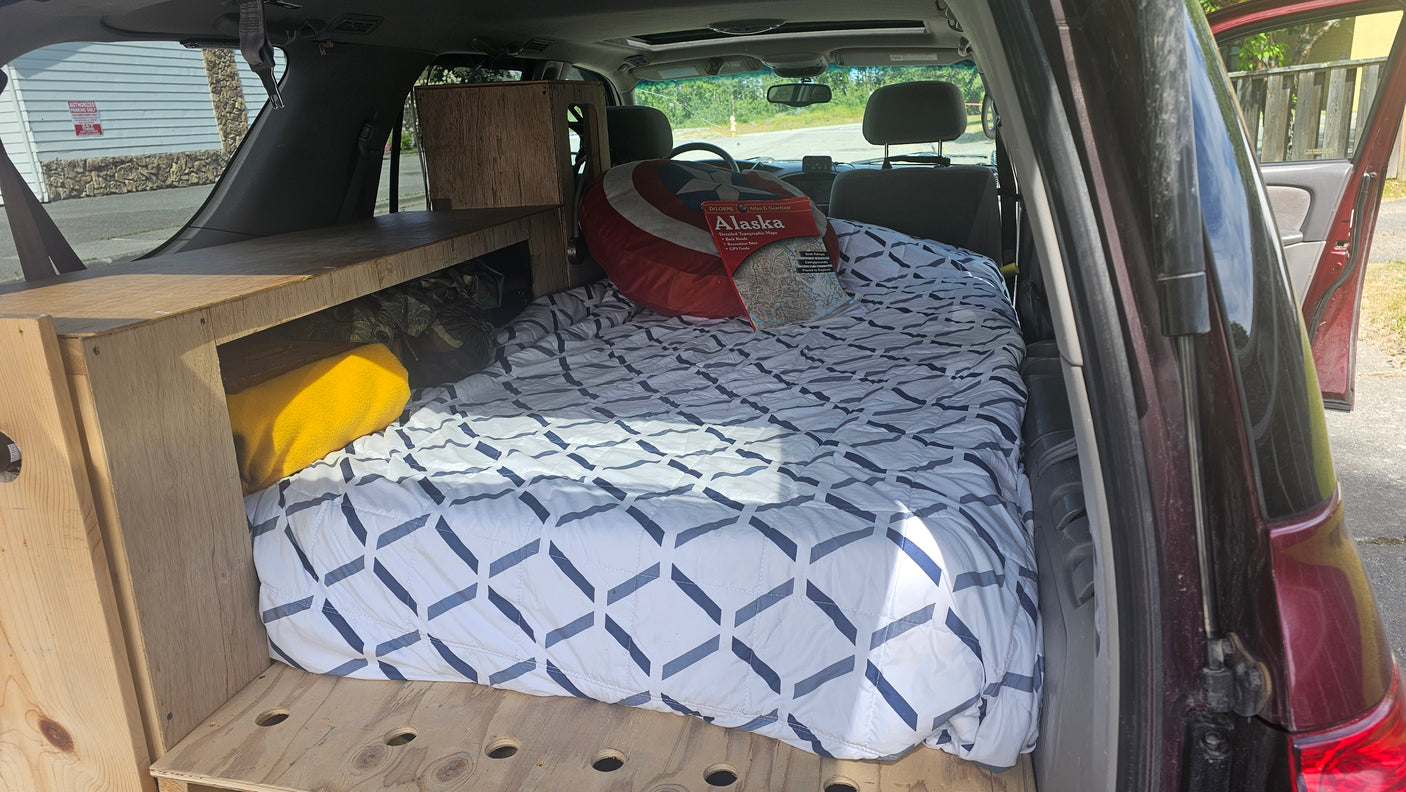 RV rental setup: A vehicle converted for car camping, featuring a comfy bed, wooden sleeping platform, and Alaska map.