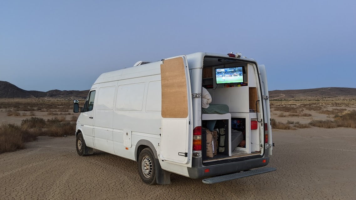 This rv rental camper van is parked in the desert, enjoying TV from inside. Ideal for van life adventure.