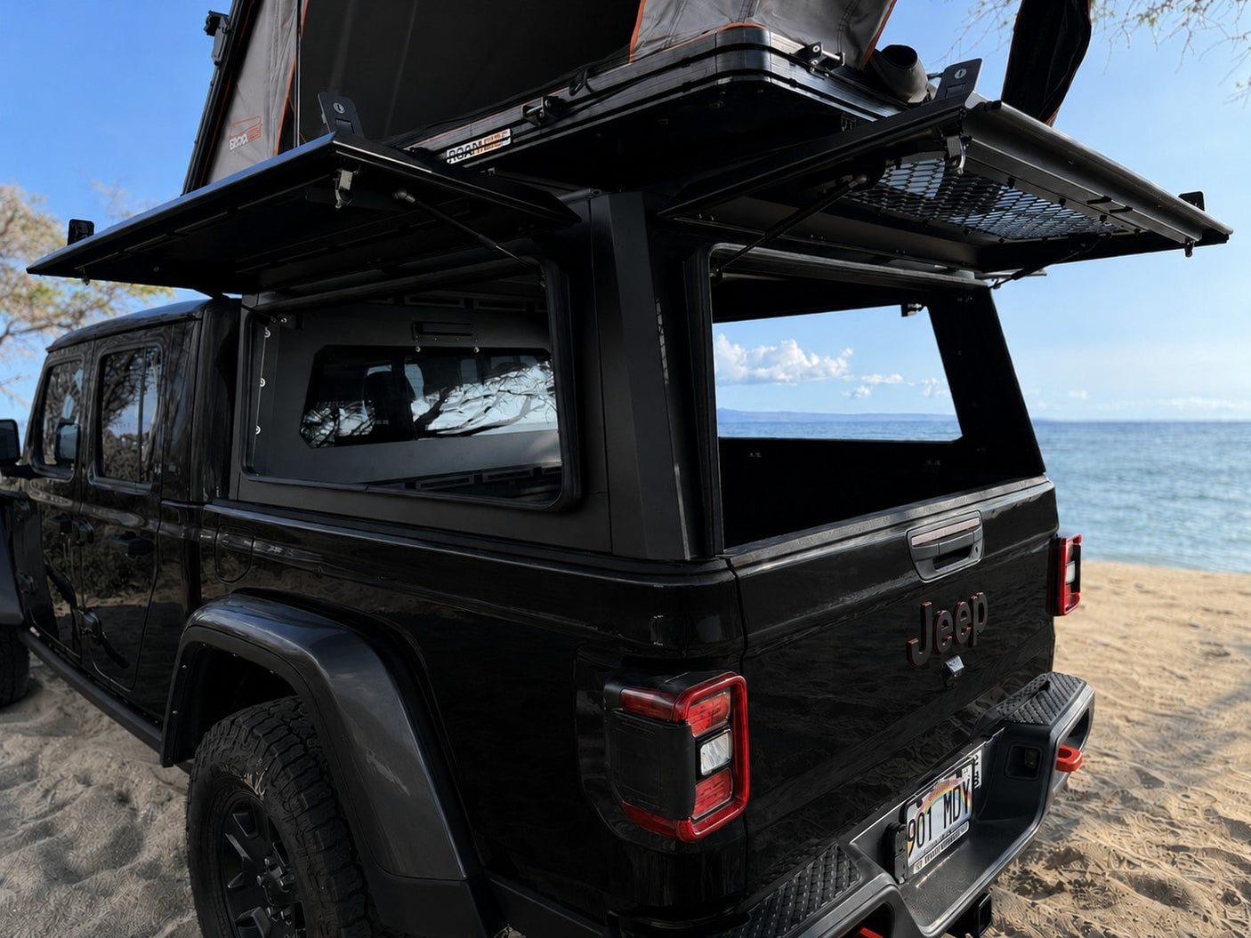 Explore with this black Jeep Gladiator RV rental! Equipped with a rooftop tent & open truck bed canopy on a sandy beach.