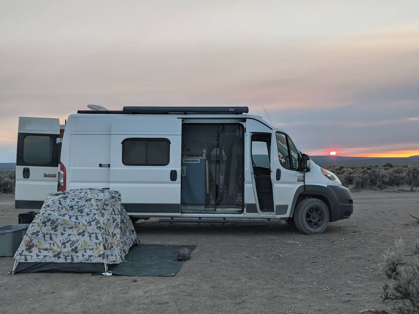 Serene sunset over an RV rental camper van and tent, parked on an open plain. Ideal for wilderness travel.