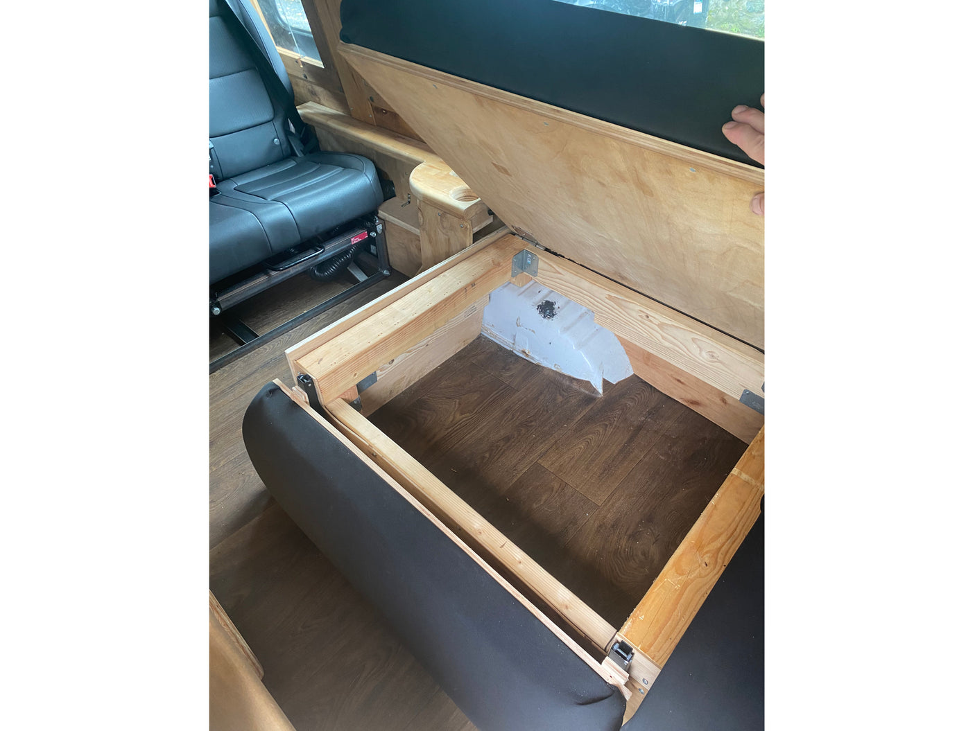 This RV rental offers clever storage: a lifted wooden platform reveals internal space beside plush seating and a vehicle seat.