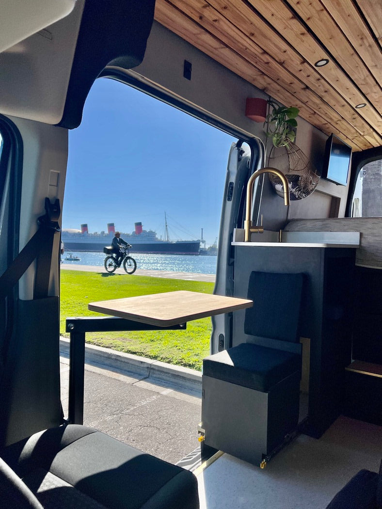 RV rental interior with wooden ceiling, table, and sink. Enjoy scenic views of the Queen Mary and bay from this camper van.