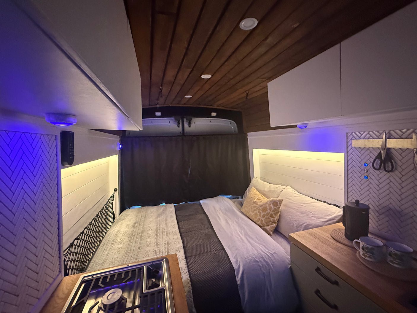 Cozy rv rental camper van interior with a comfy bed, compact kitchen, and inviting ambient lighting.
