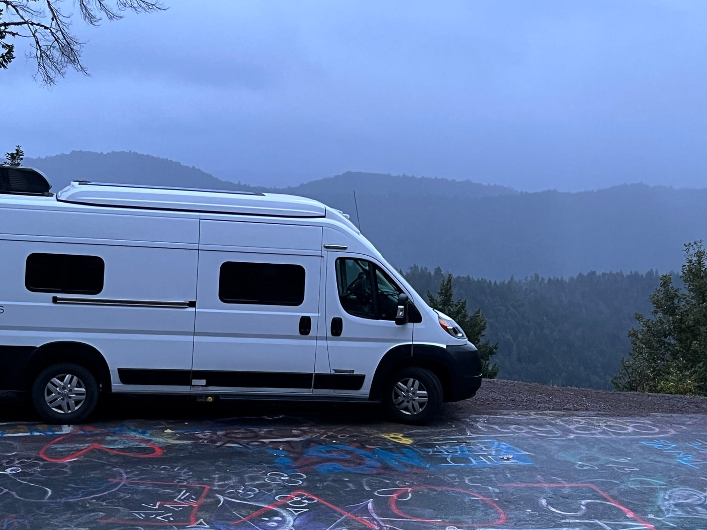 Scenic RV rental parked with a misty mountain backdrop. Graffiti covers the ground, enhancing this unique travel view.