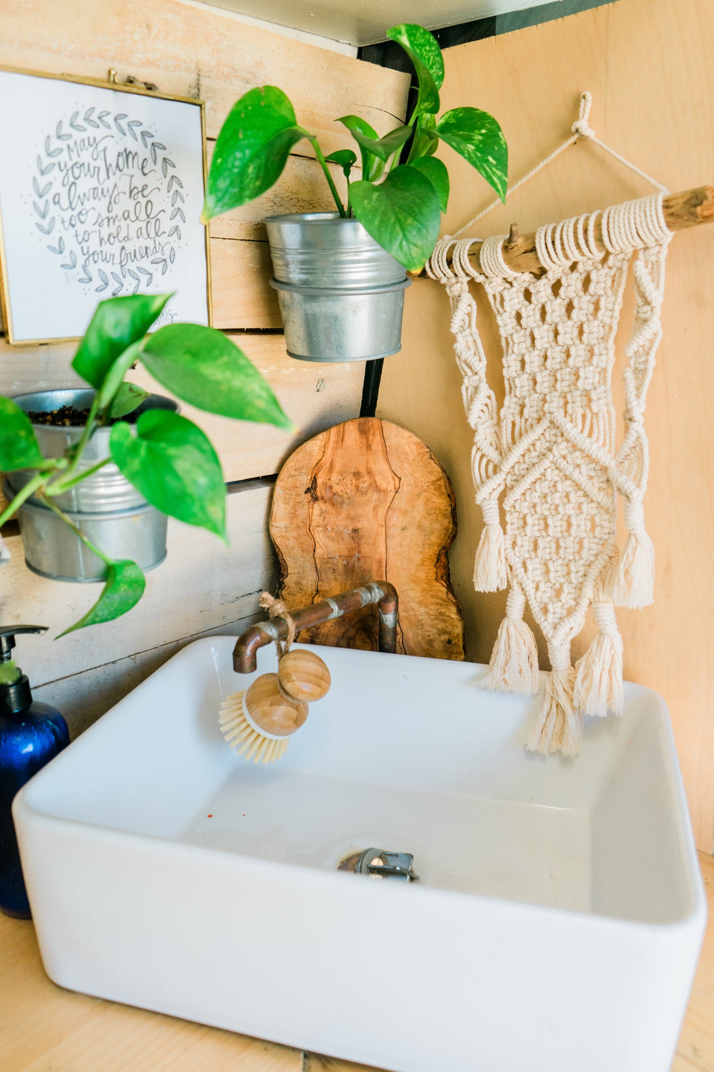 Cozy RV rental interior featuring a white sink, unique copper faucet, macrame decor, and potted plants for a homely touch.