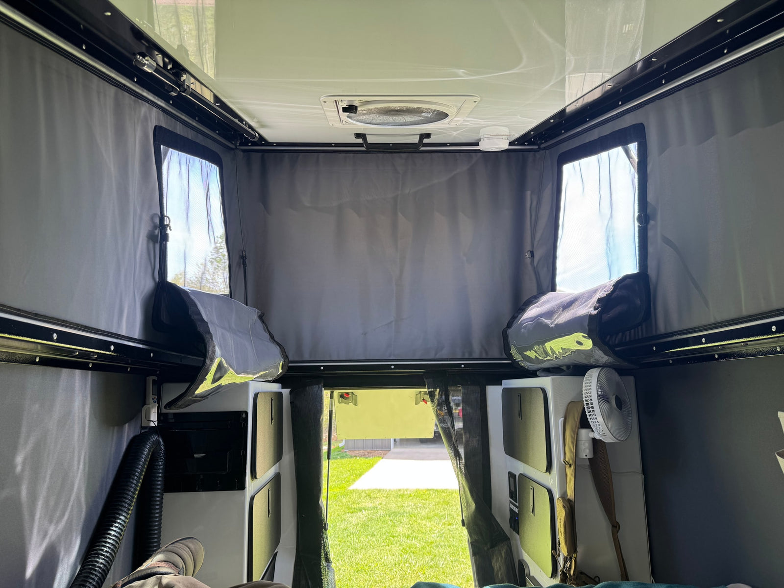 Interior of an rv rental pop-top camper, with ceiling fan, mesh windows, storage, and outdoor view.