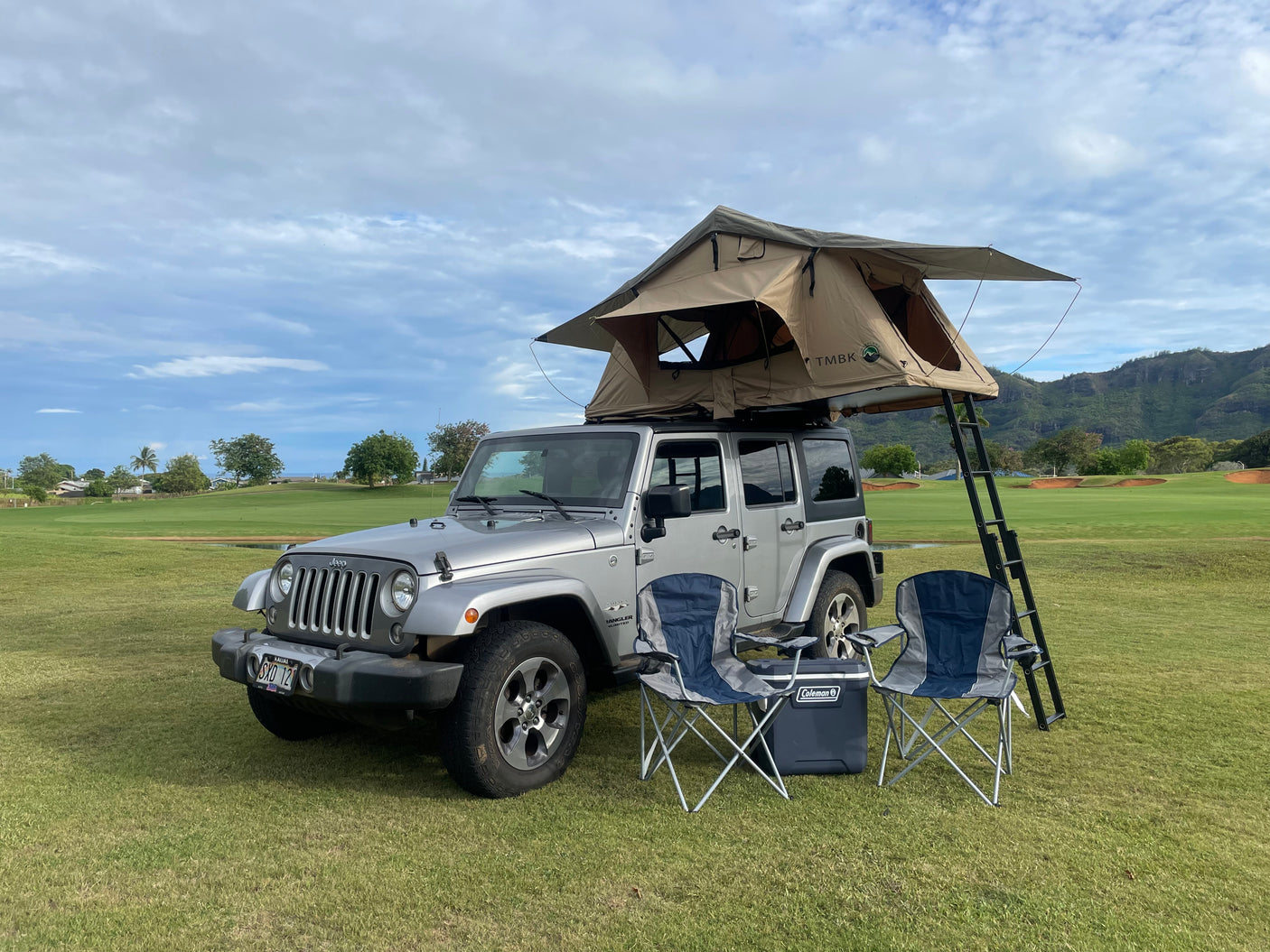 Silver Jeep Wrangler with TMBK rooftop tent, camping chairs, and cooler. Perfect RV rental for outdoor adventures.