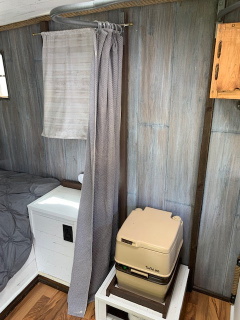 Inside your RV rental: a compact layout with a portable toilet, privacy curtain, and cozy bed.