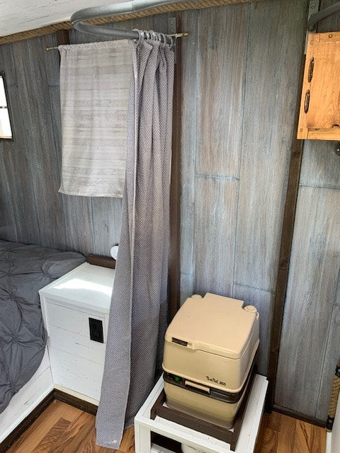 Inside your RV rental: a compact layout with a portable toilet, privacy curtain, and cozy bed.