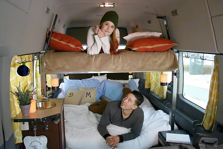 This cozy rv rental interior features a woman on the upper bunk and a man on the lower bed