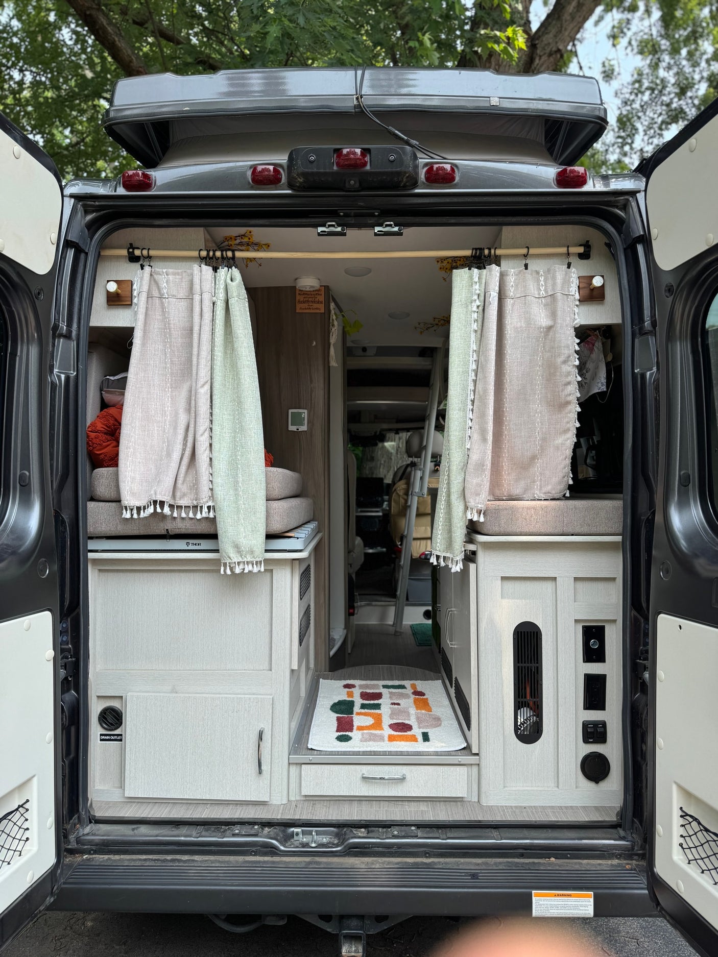 This RV rental shows the functional and cozy interior of a camper van with rear doors open, featuring a bed, kitchen, and controls.