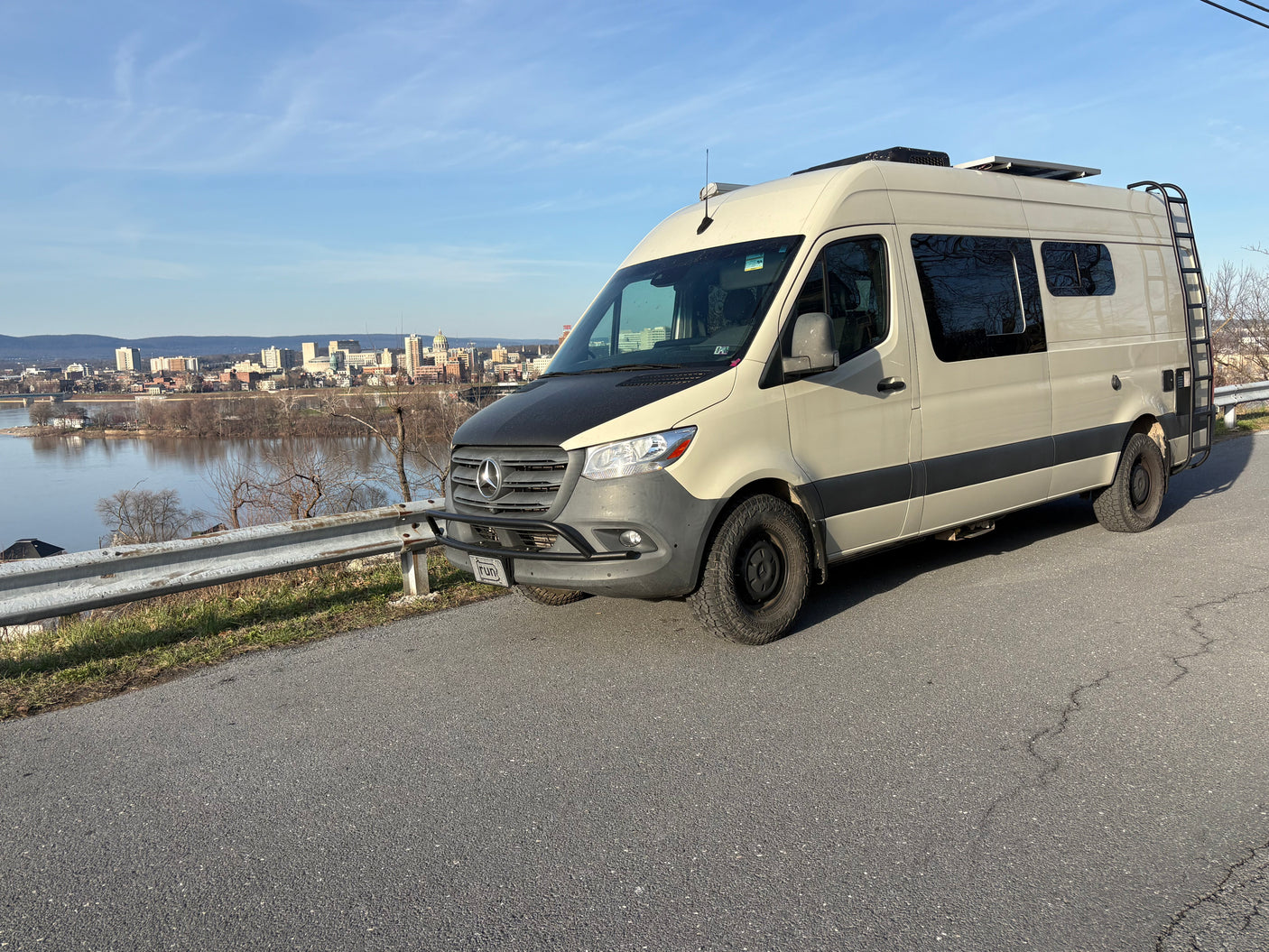 Adventure-ready Mercedes Sprinter camper van, ideal for RV rental, overlooks a scenic city and river.