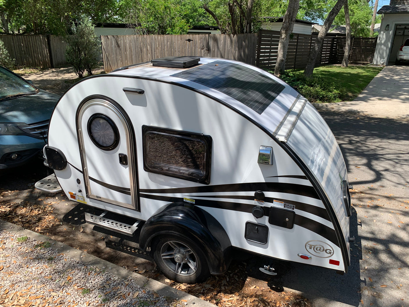 White T@G teardrop trailer with black stripes and solar panels, perfect for an RV rental adventure, parked outside.