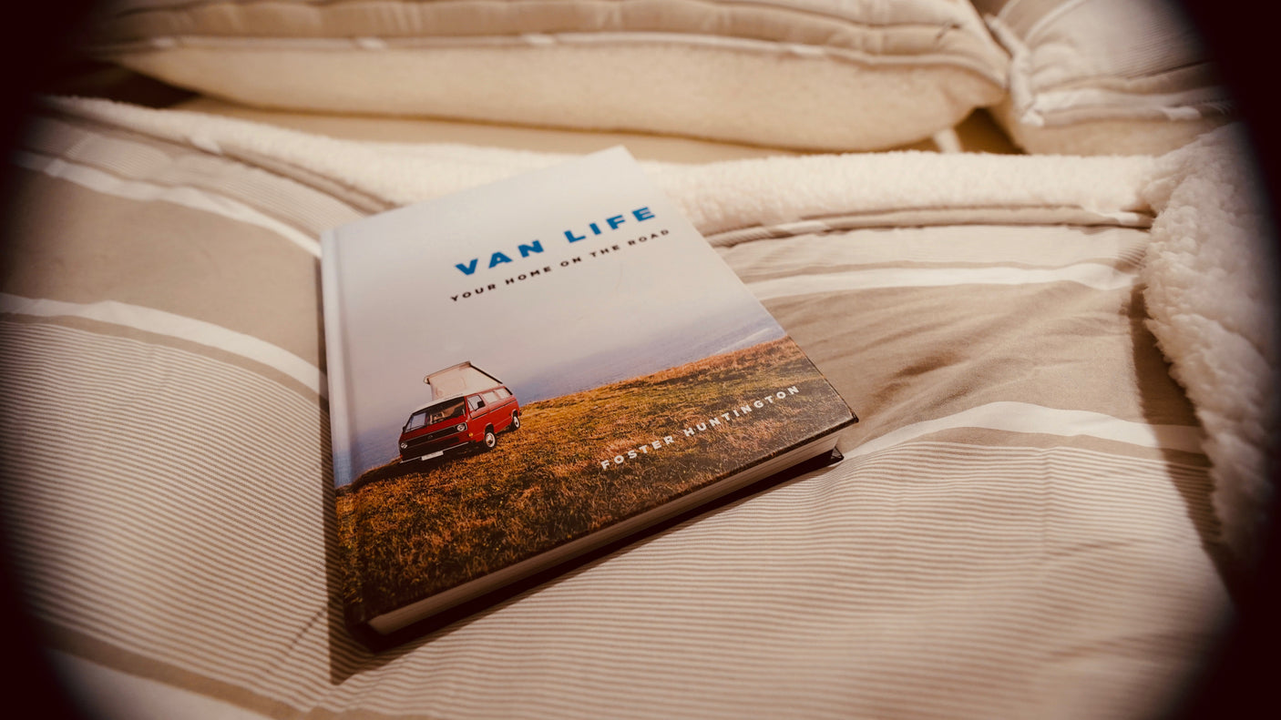A "Van Life" book featuring a red camper van rests on cozy, striped bedding. Perfect for planning your next rv rental adventure.